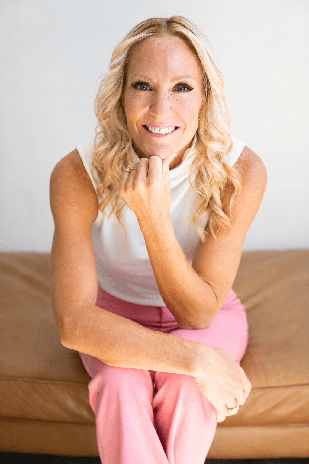 Amy Sanders sitting on a leather bench, chin resting on her hand, smiling