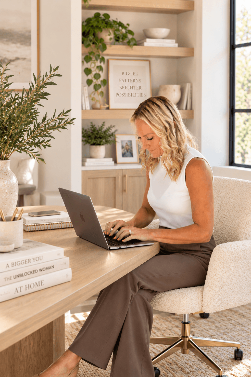 Amy Sanders at her desk, typing on her laptop, a “Bigger Patterns, Brighter Possibilities” print on the shelf behind her