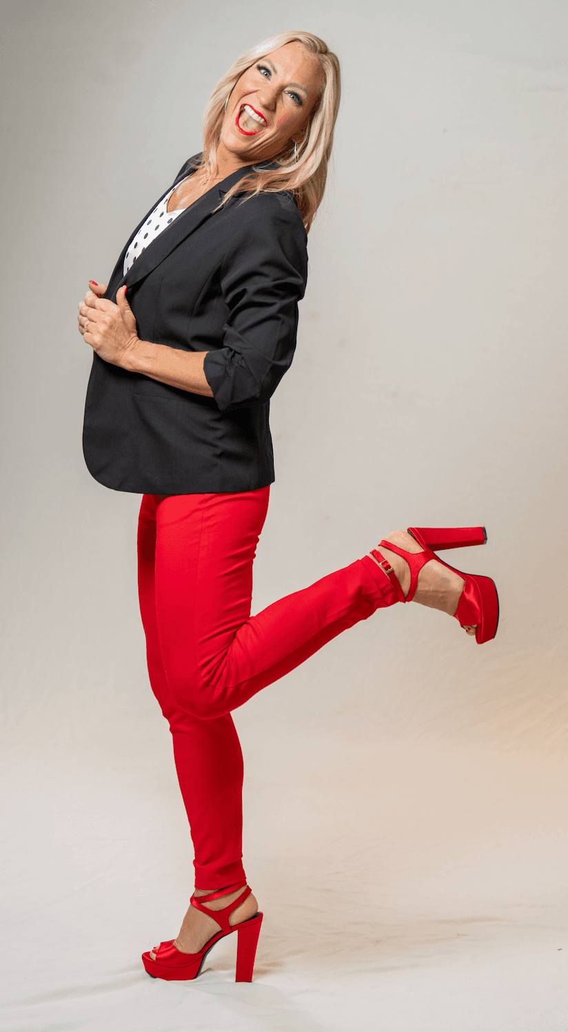 Amy Sanders kicking one heel up, in a black blazer and red pants