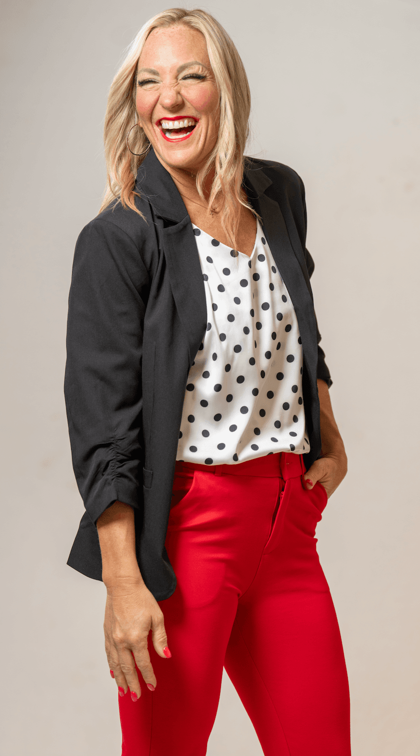 Amy Sanders laughing, in a black blazer and red pants